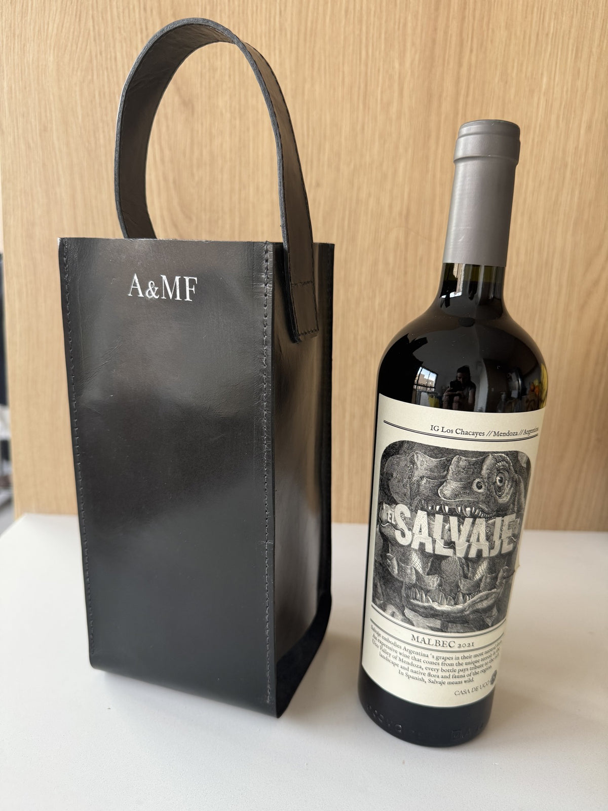 Wine bag de couro preta com garrafa de vinho ao lado